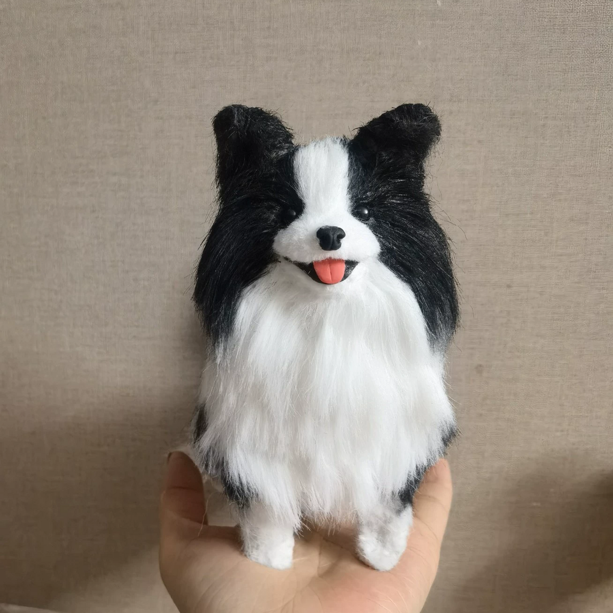 Black and white dog toy held in a hand against a beige background