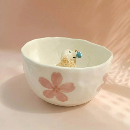 Small dog figurine inside a white bowl with pink floral design on a soft pink background