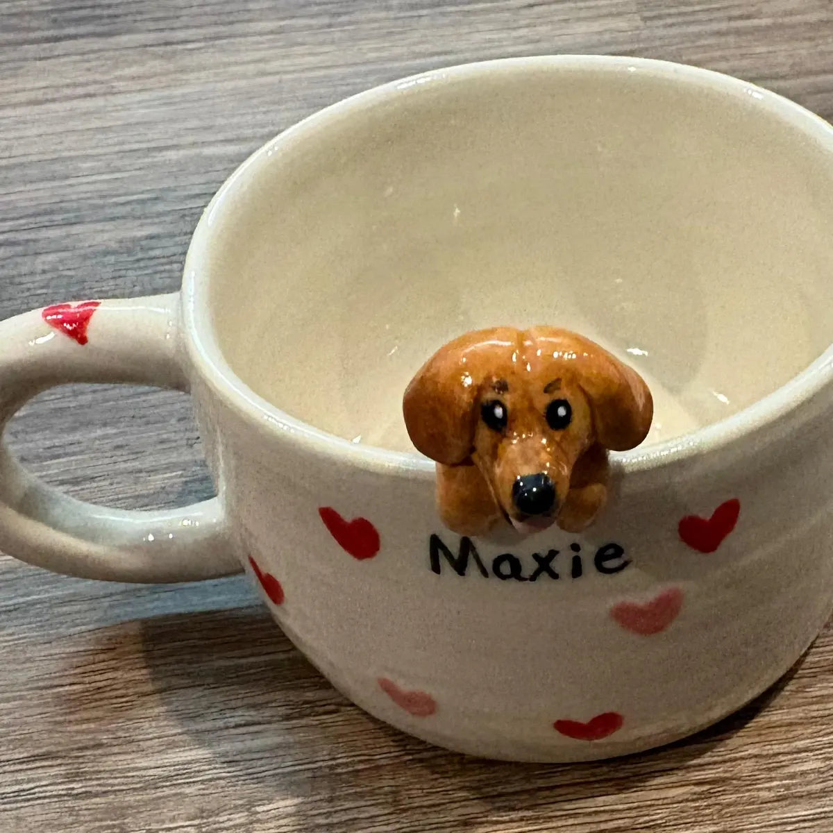 White mug with 'Maxie' and heart designs, containing a small brown dog figurine.