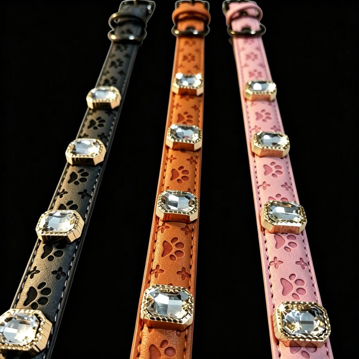 Three dog collars in black, brown, and pink with paw prints and gemstones on a black background.