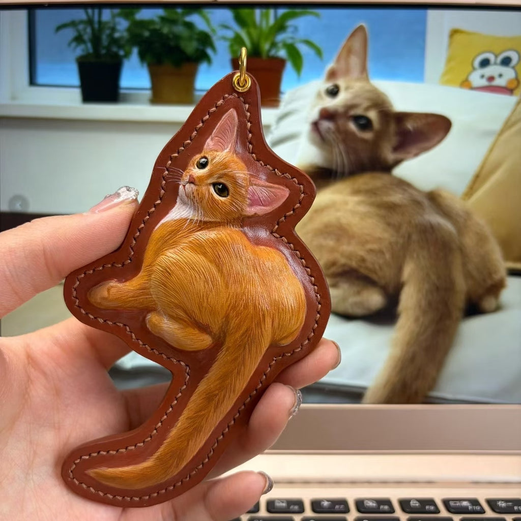 Hand holding a custom pet leather cat-shaped keychain with a cat in the background