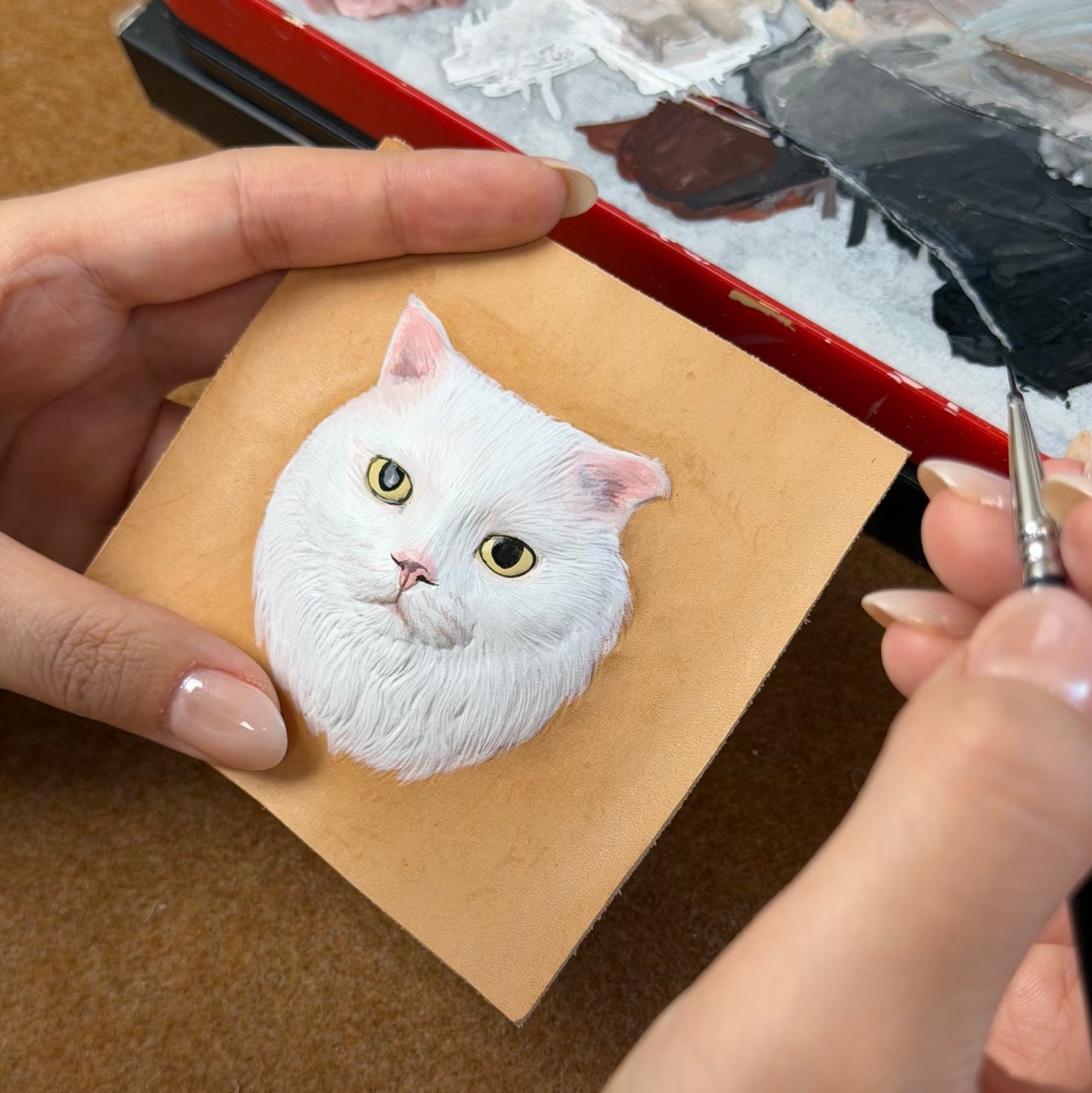 Artistic depiction of a white cat's face on a leather with a brush nearby.