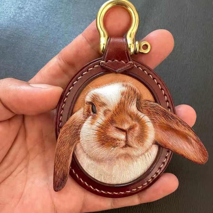 Custom Leather Oval Pet Portrait Keychain with a rabbit design held in a hand against a dark background