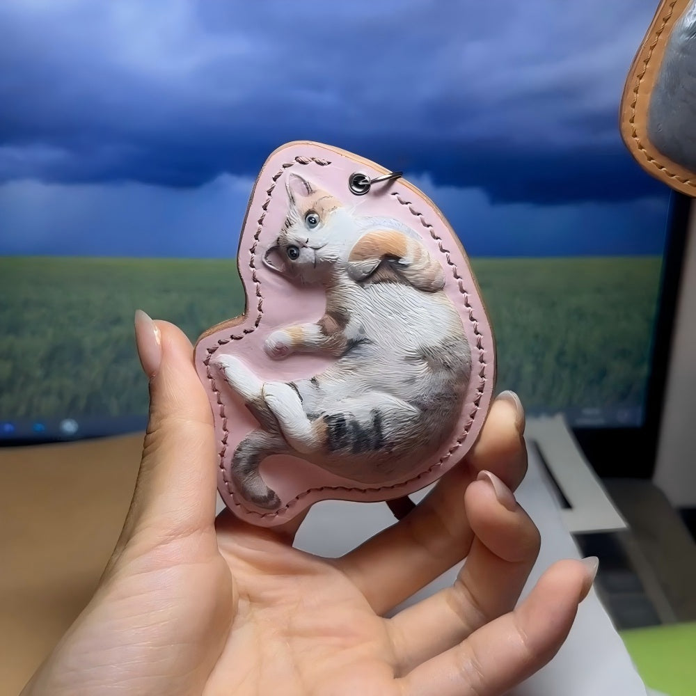 Hand holding a pink Leather Pet Portrait Keychain with a cat design against a computer screen background.