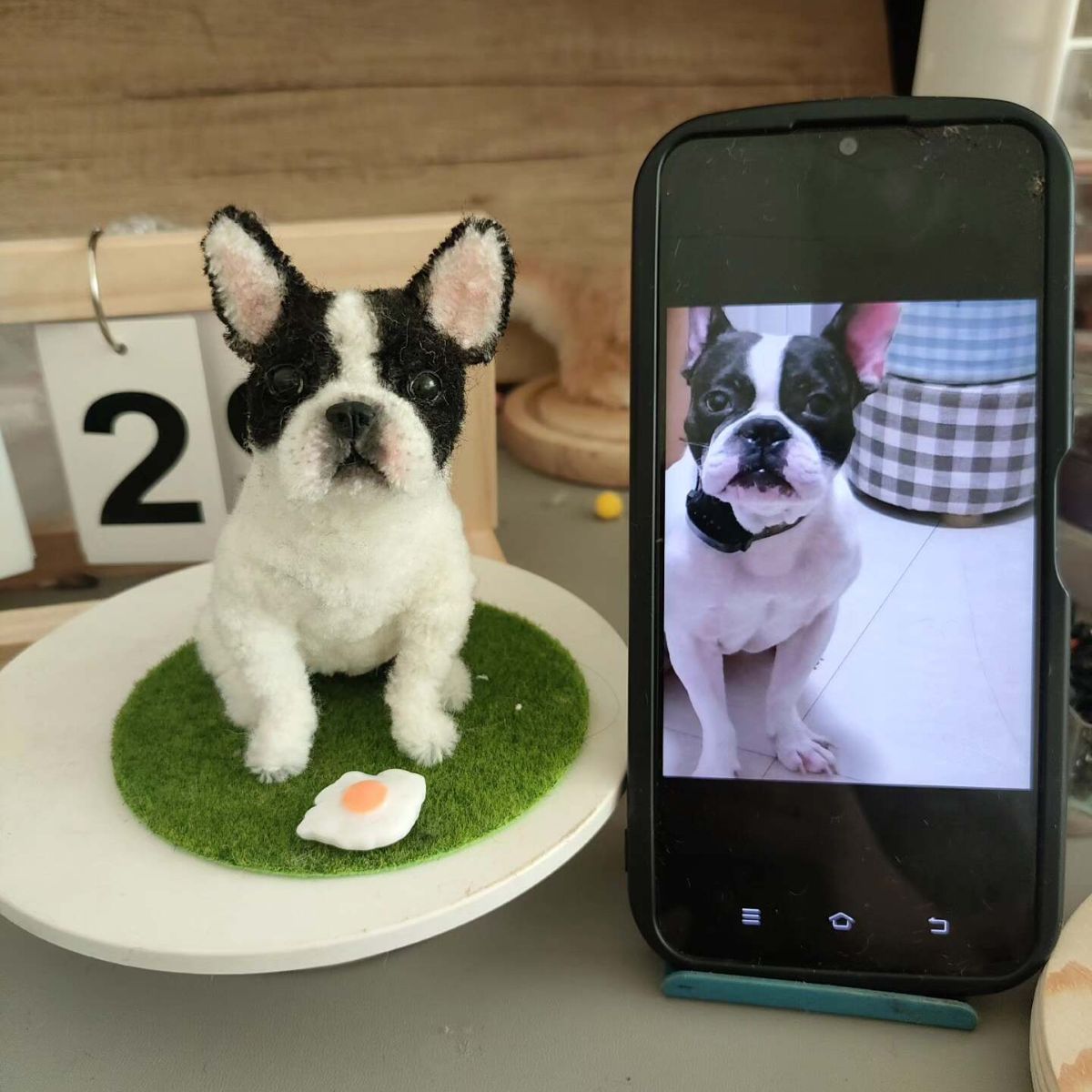 Small black and white dog on a green rug next to a smartphone displaying a video call with another dog.