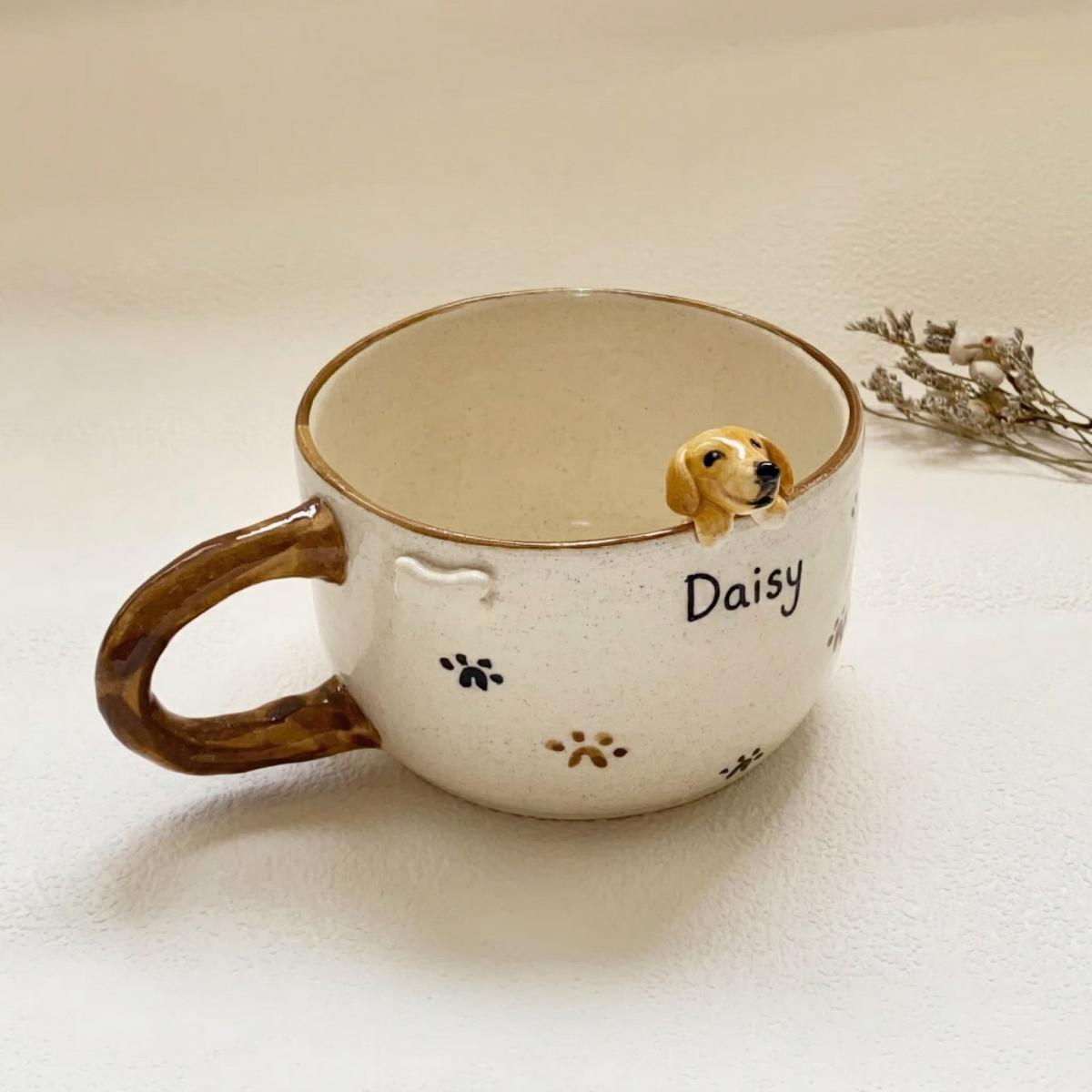 Ceramic mug with a small dog figurine and 'Daisy' written on it, on a light background.