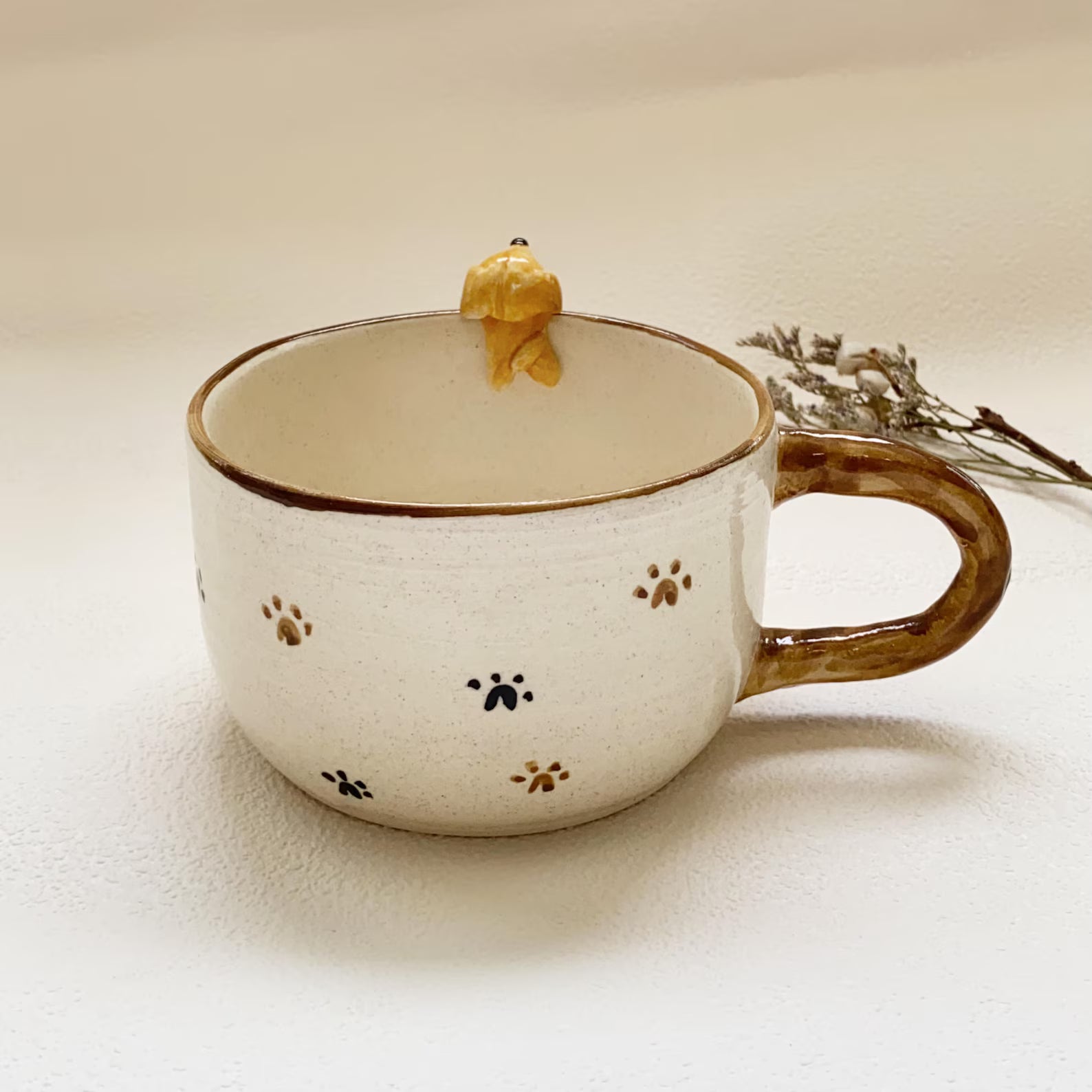 Ceramic mug with brown handle and decorative paw prints on a beige background