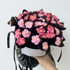 Bouquet of pink and yellow crocheted flowers in a black wrap with a white background