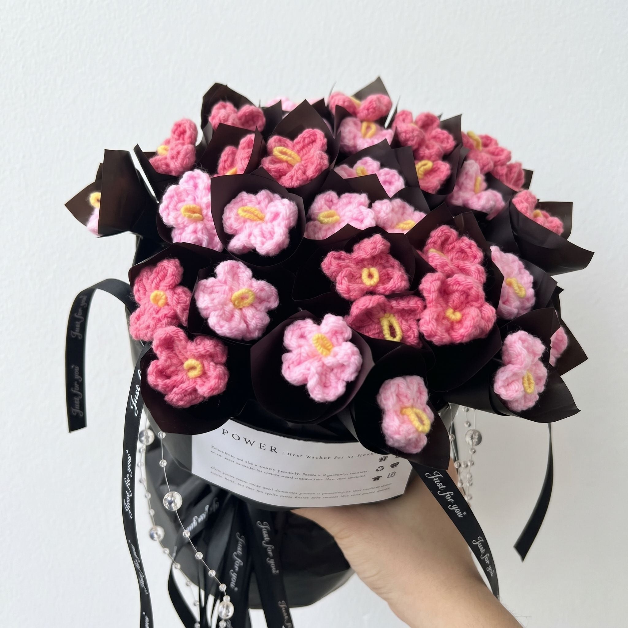 Bouquet of pink and yellow crocheted flowers in a black wrap with a white background