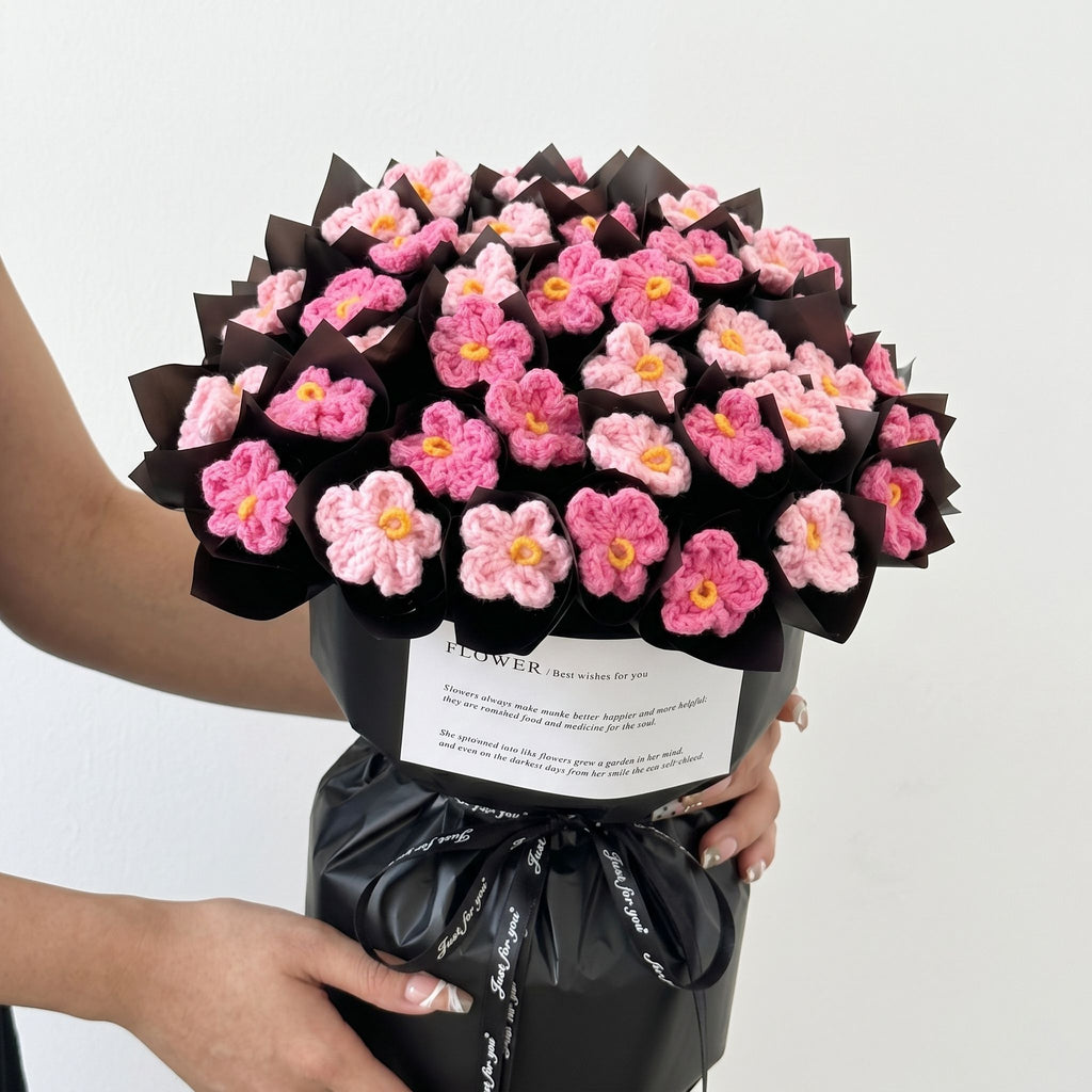 Bouquet of pink flowers wrapped in black paper held by a person against a white background