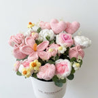 Crocheted flower arrangement in a white pot with 'The Rosemada' branding on a light gray background.