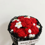 Crocheted red flowers in a black pot with a white card below on a light gray background