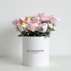 White cylindrical box with 'The Rosemadam' branding containing knitted flowers on a light gray background