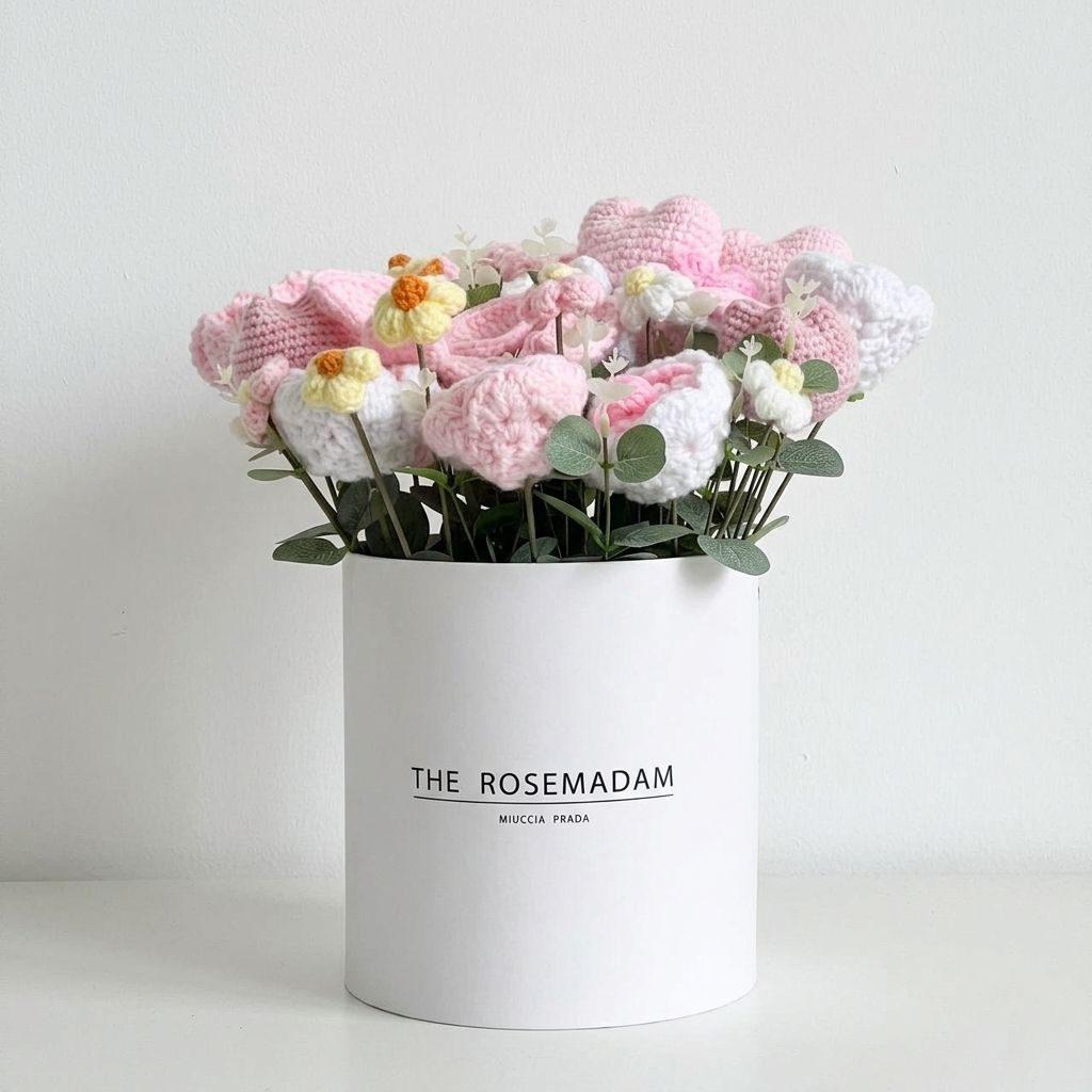 White cylindrical box with 'The Rosemadam' branding containing knitted flowers on a light gray background