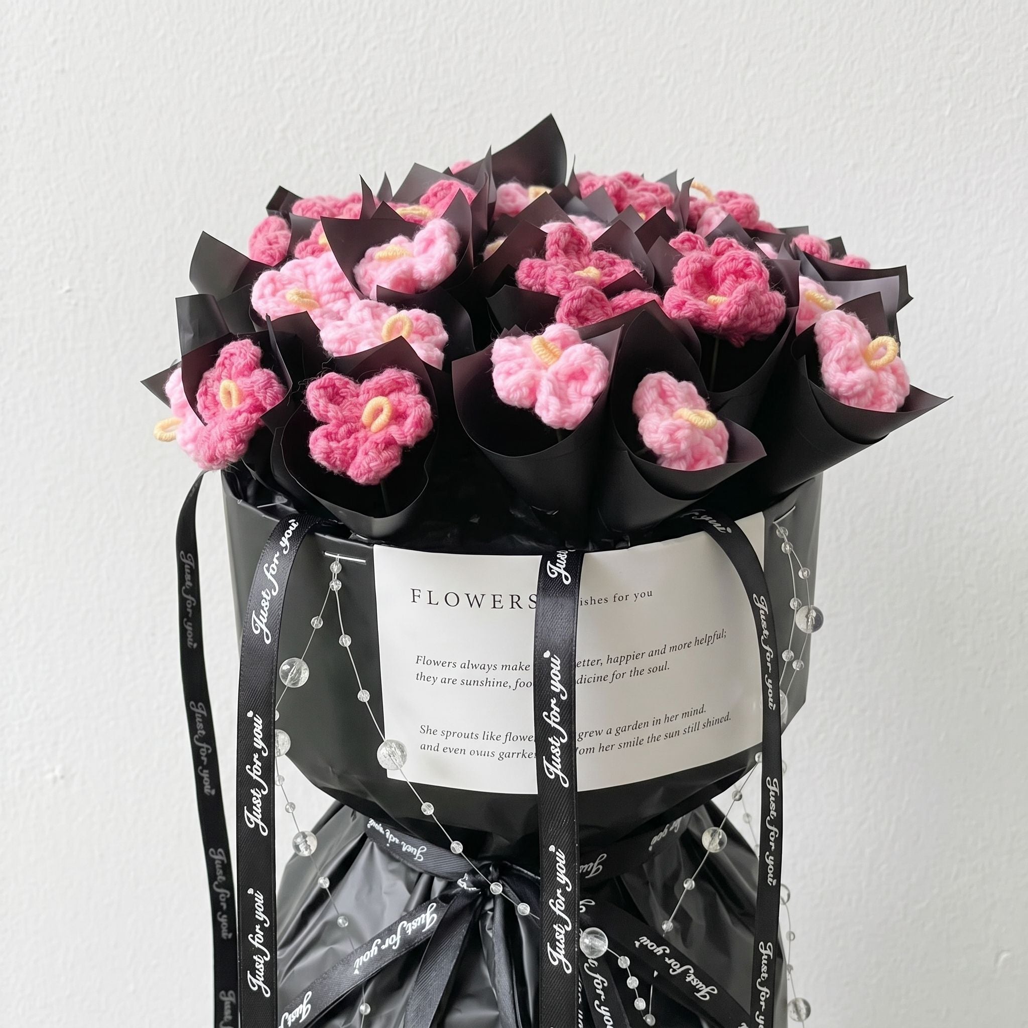 Bouquet of pink flowers wrapped in black paper with a white label on a light gray background