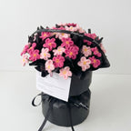 Bouquet of pink flowers wrapped in black paper with a card on a white background