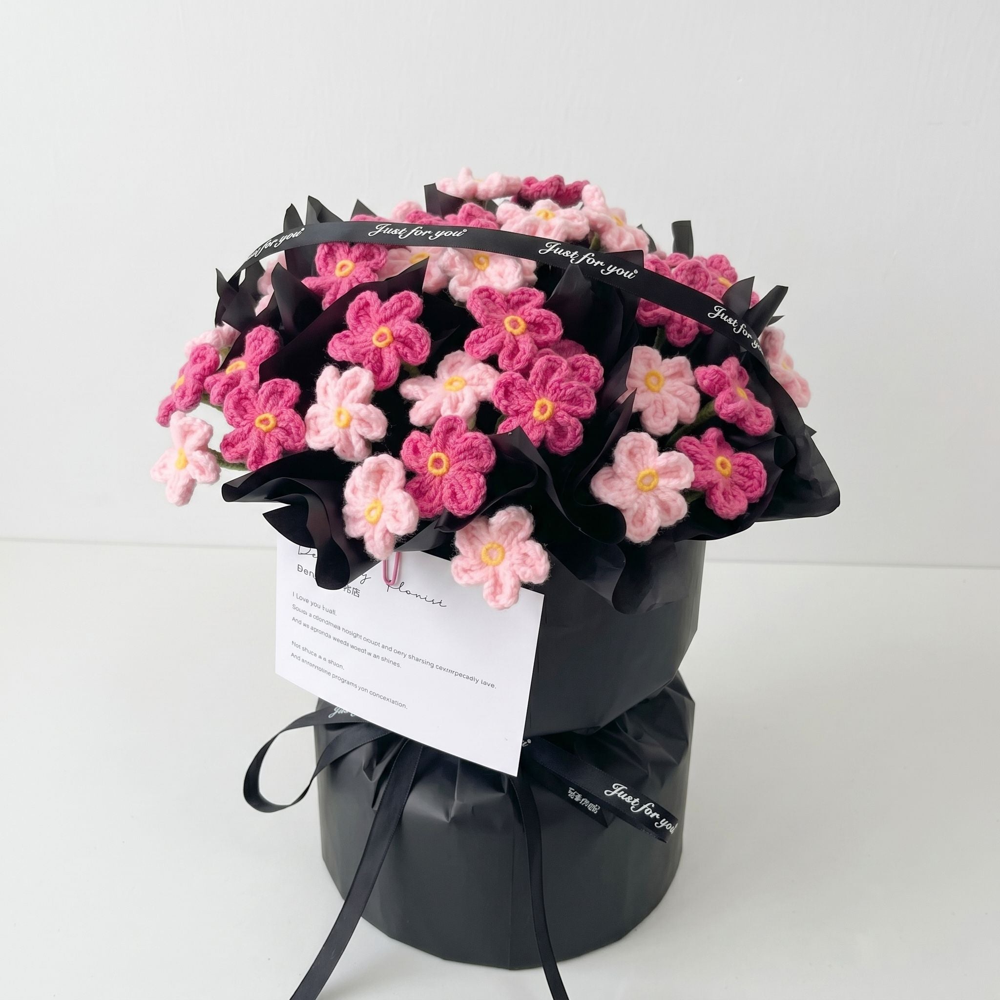 Bouquet of pink flowers wrapped in black paper with a card on a white background