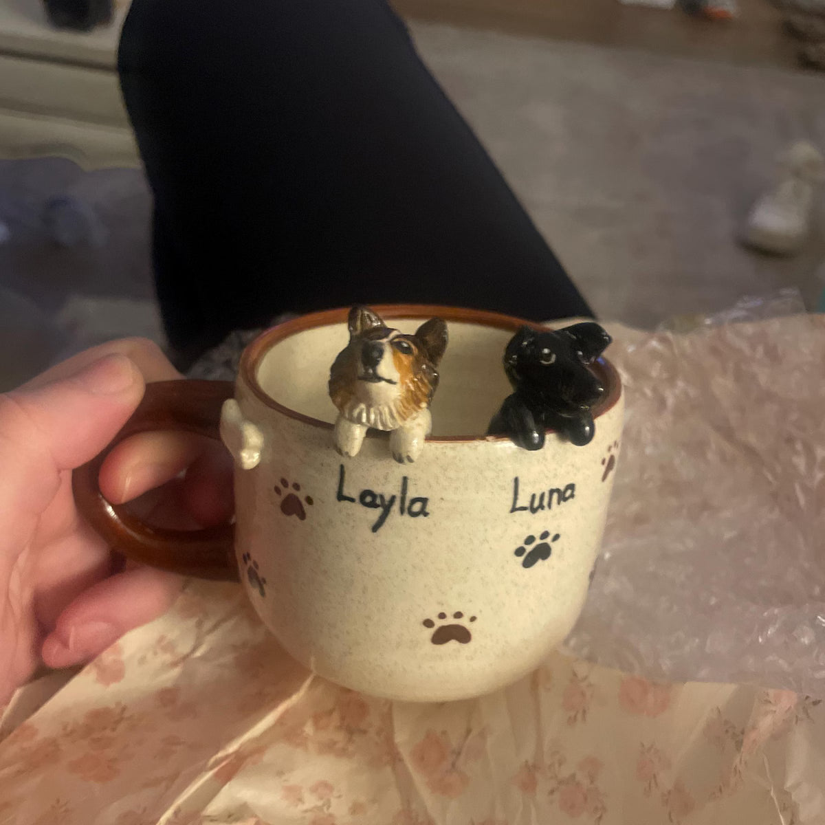Ceramic mug with dog figurines and names 'Layla' and 'Luna' on a floral tablecloth.