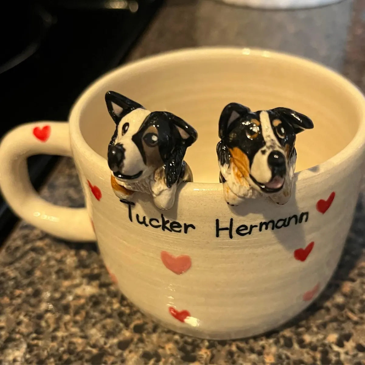 Mug with dog-shaped earrings and 'Tucker Hermann' text on a countertop.