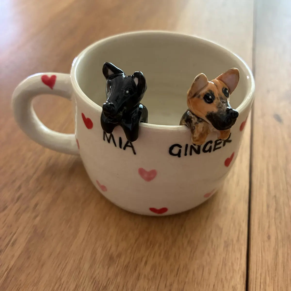 Mug with dog figurines and names 'Mia' and 'Ginger' on a wooden surface