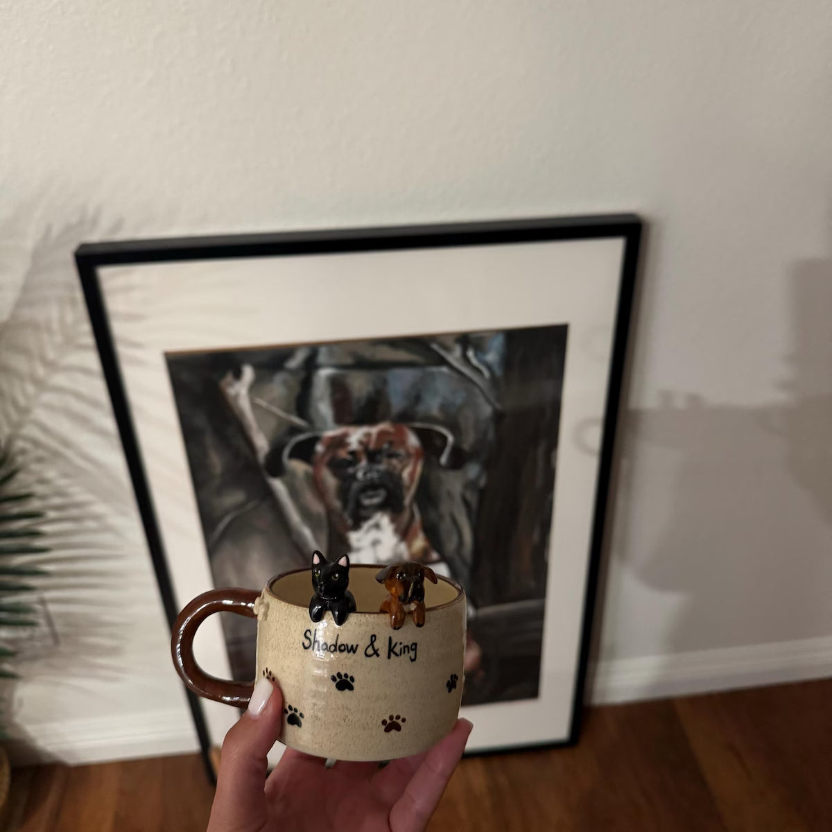 Person holding a mug with dog figurines in front of a framed picture of a dog.