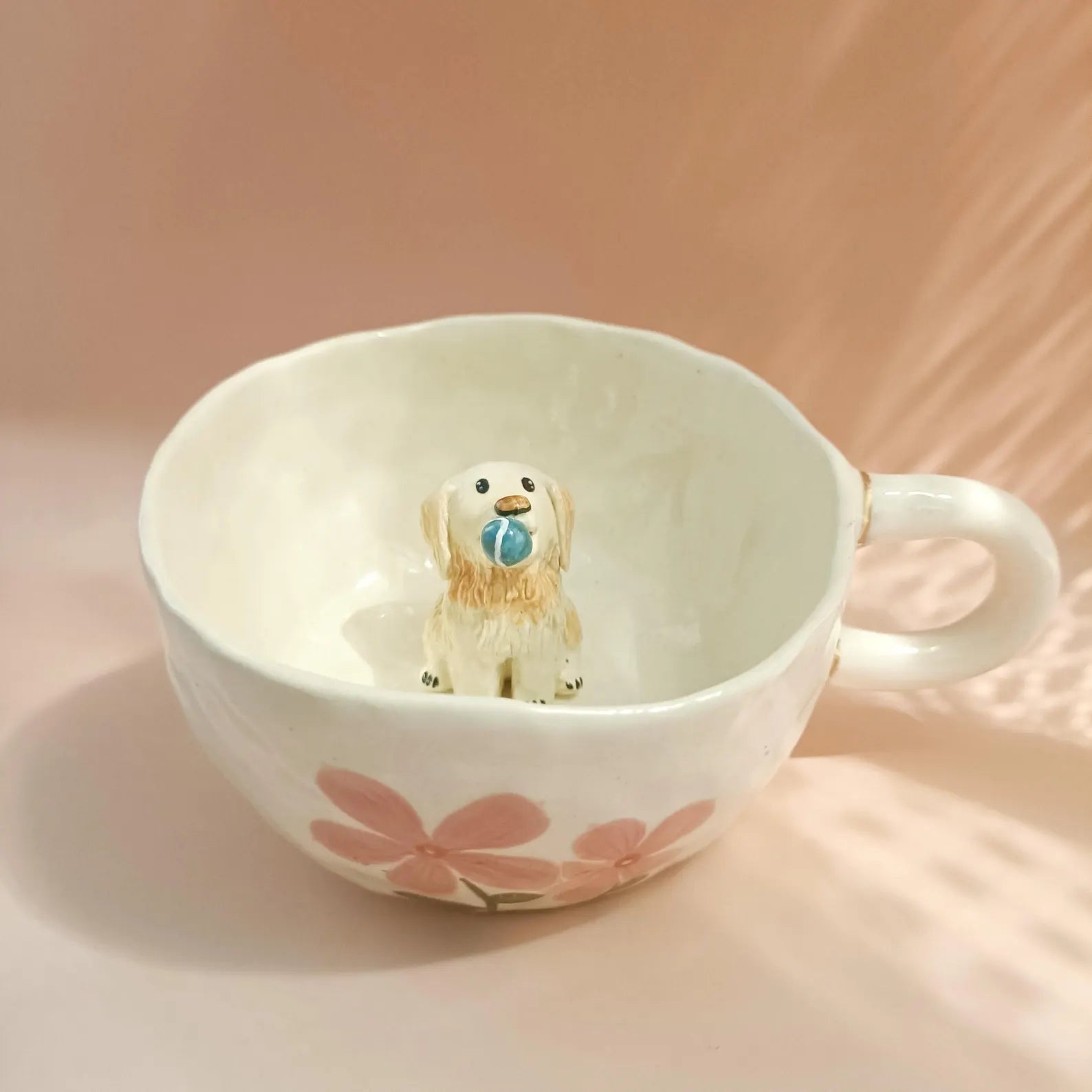 Small dog figurine inside a floral-patterned mug on a soft pink background