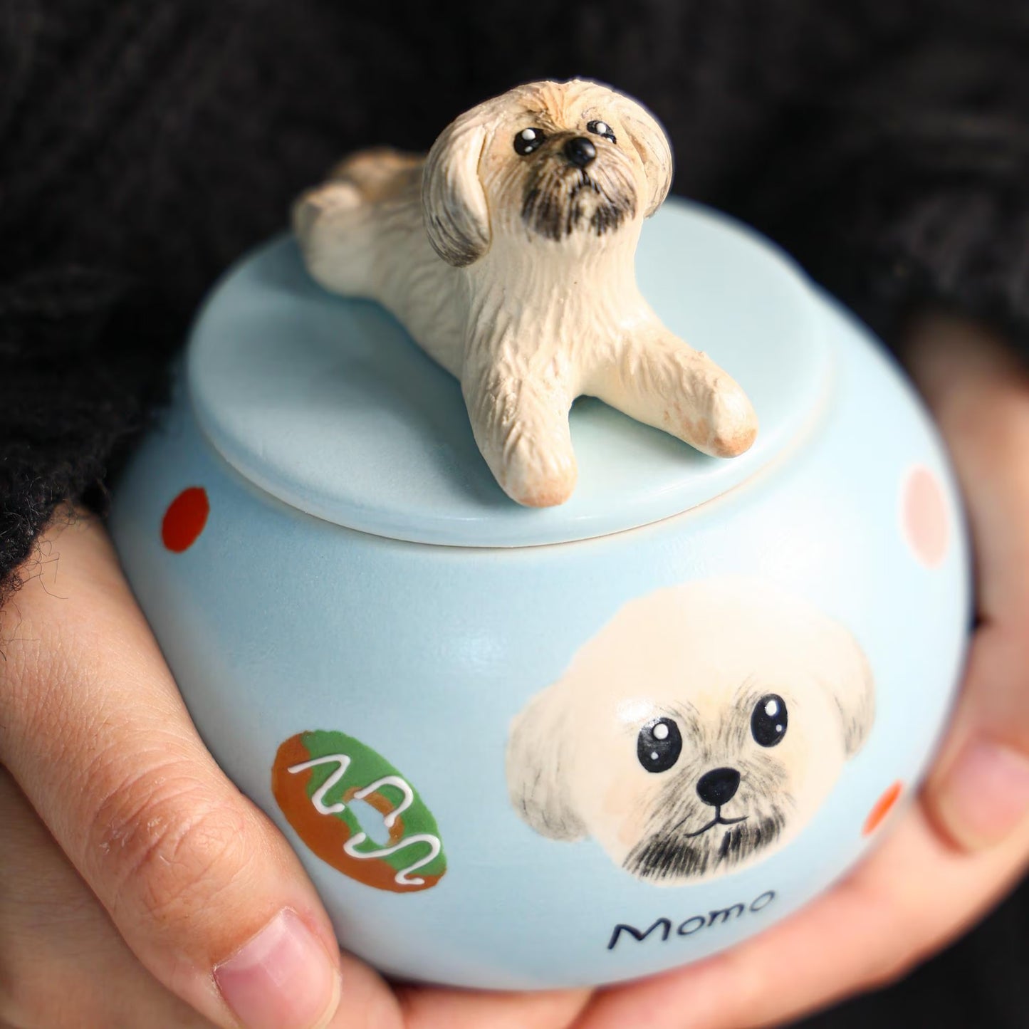 Ceramic urn with a dog figurine on top held by hands