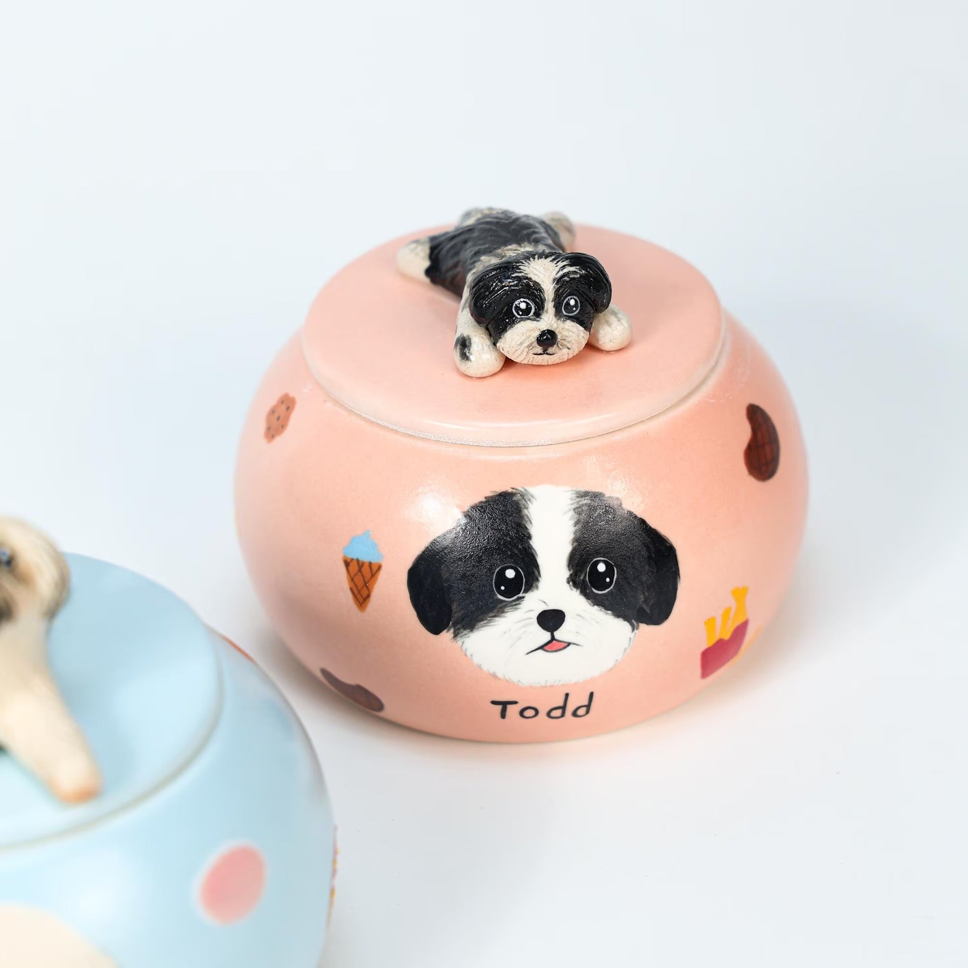 Pink ceramic urn with a black and white dog design and a small dog figurine on top, on a light background.