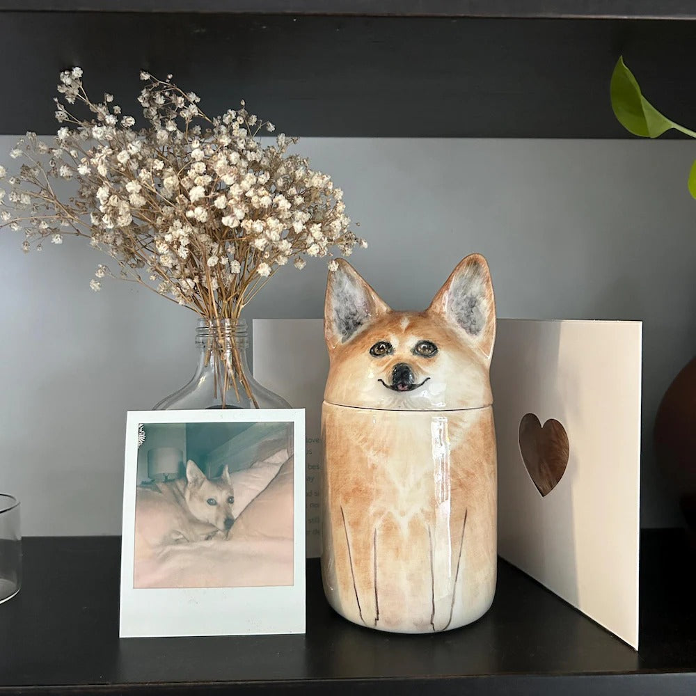 Ceramic dog-shaped urn on a shelf with a photo and dried flowers.
